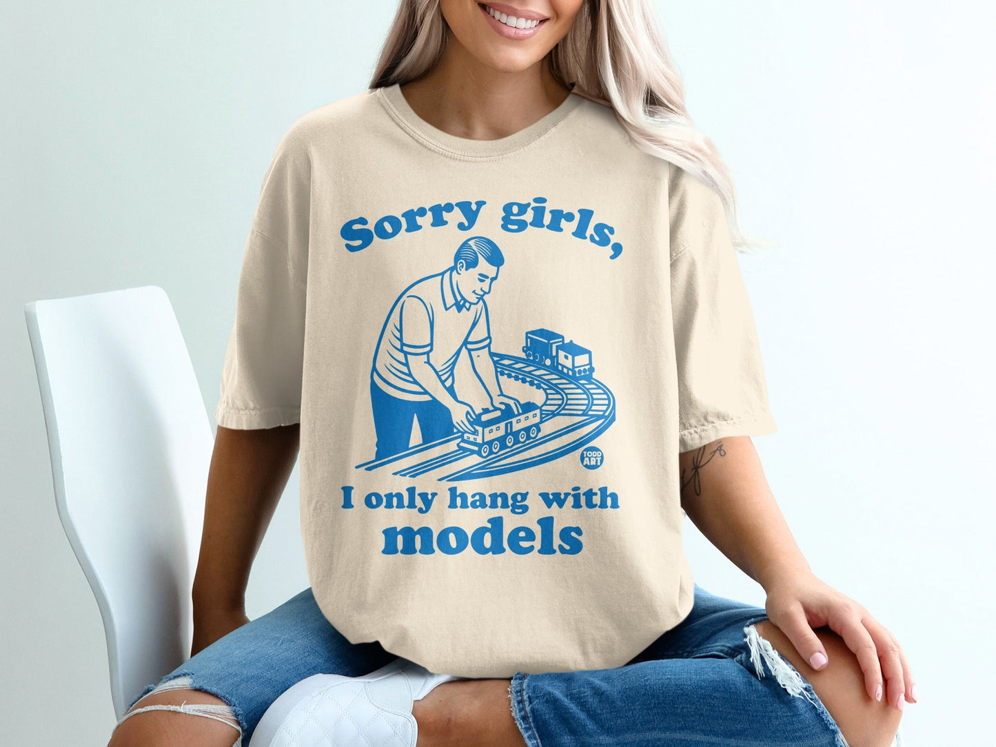 Beige t-shirt with blue text and graphic of a man with a model train set.