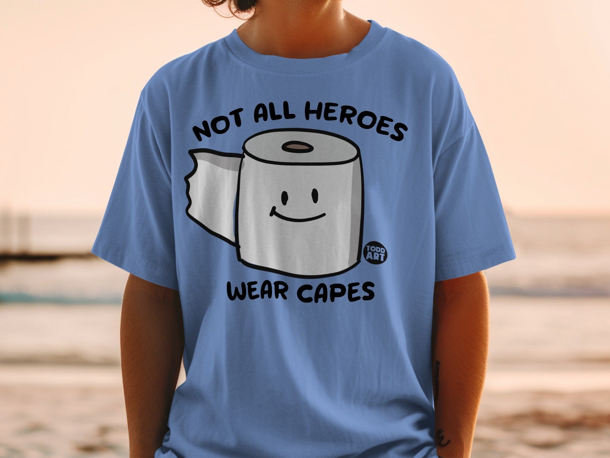 Blue t-shirt with a roll of toilet paper graphic that says "Not all heroes wear capes".