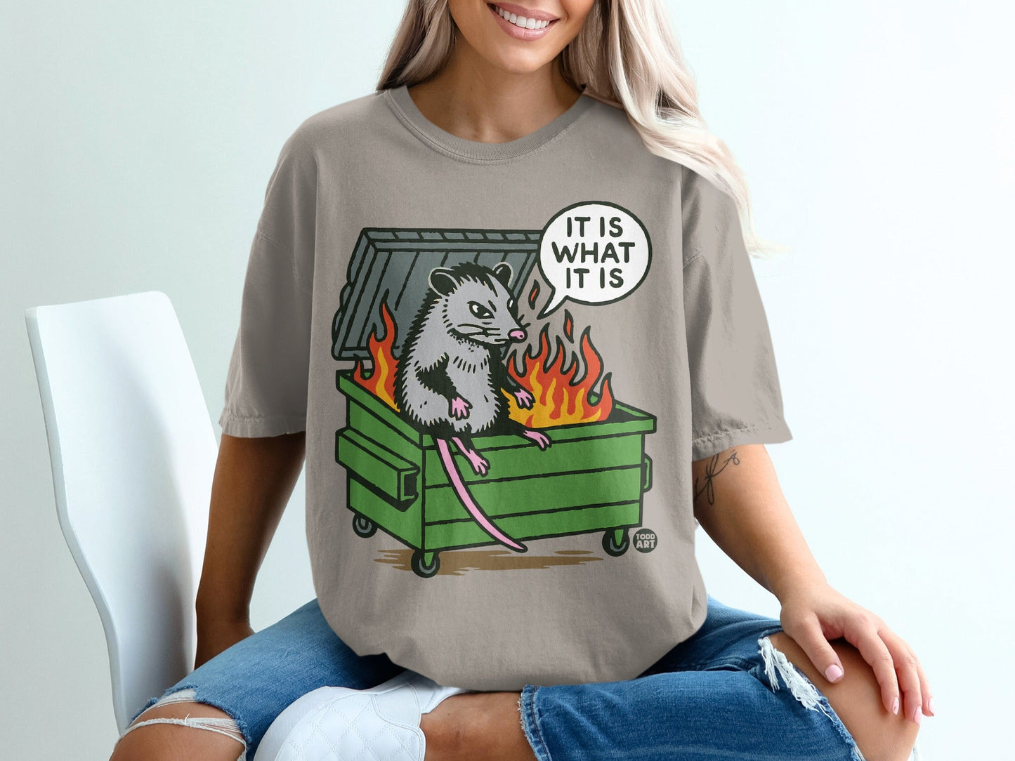 Opossum sitting in a burning dumpster, speech bubble says "It is what it is".