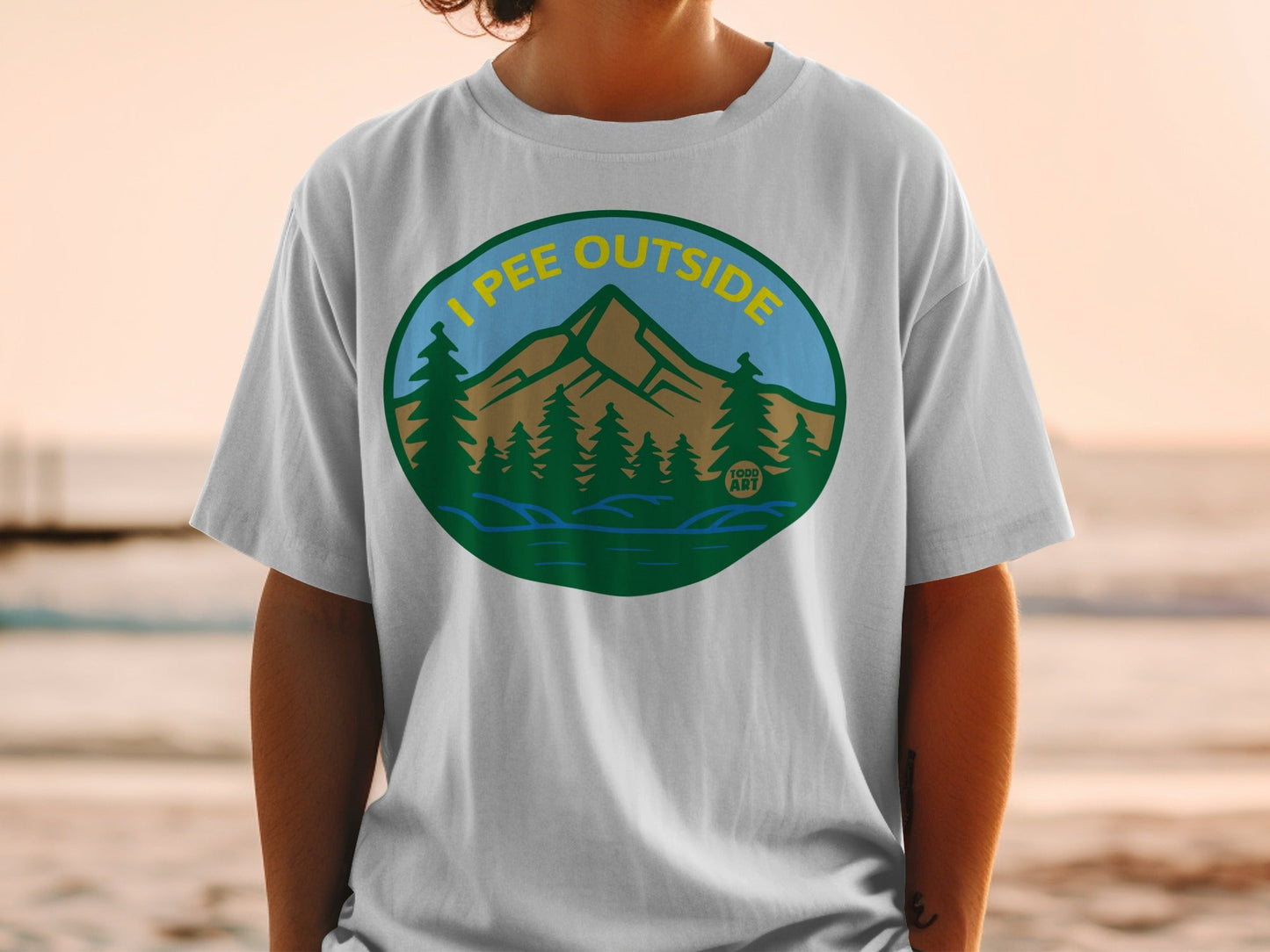 Circular graphic on t-shirt with mountains, trees, and "I PEE OUTSIDE" text.