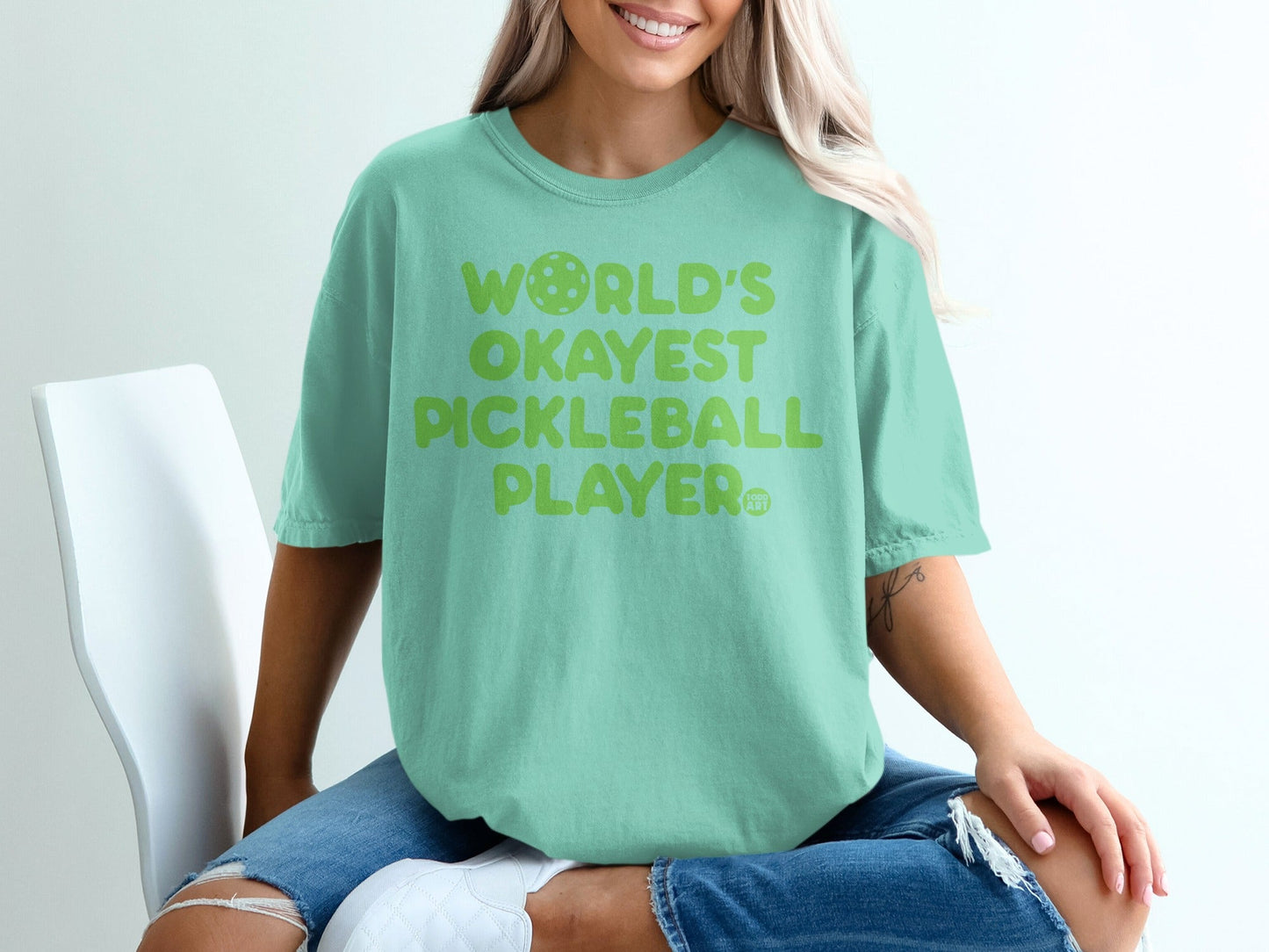 Mint green t-shirt with "World's Okayest Pickleball Player" text and pickleball graphic.
