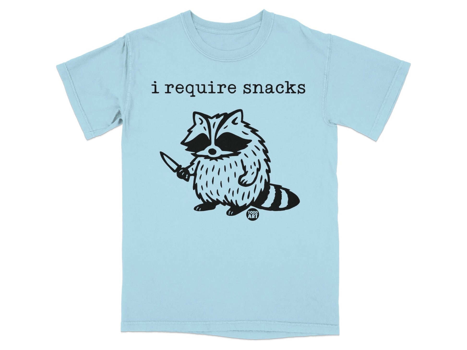 Light blue t-shirt with black graphic of a raccoon holding a knife and text "i require snacks".