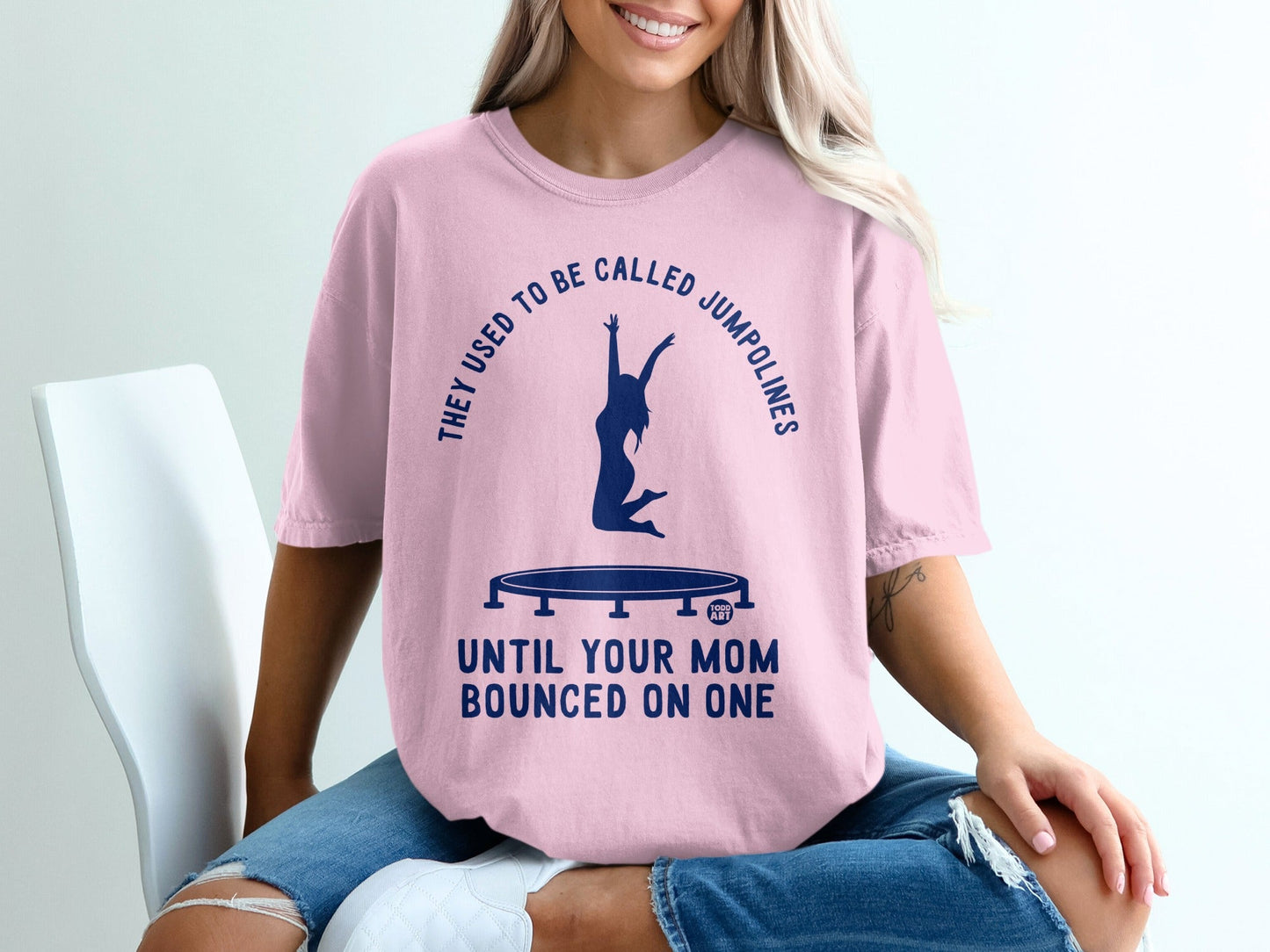Pink t-shirt with graphic of a woman jumping on a trampoline and text.