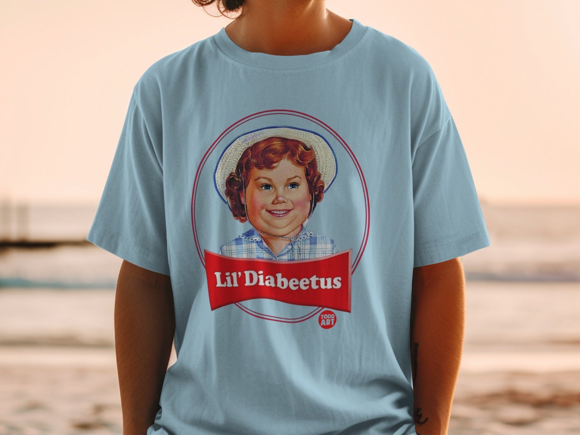 Light blue t-shirt featuring a circular logo with a young girl's portrait and "Lil' Diabeetus" text.