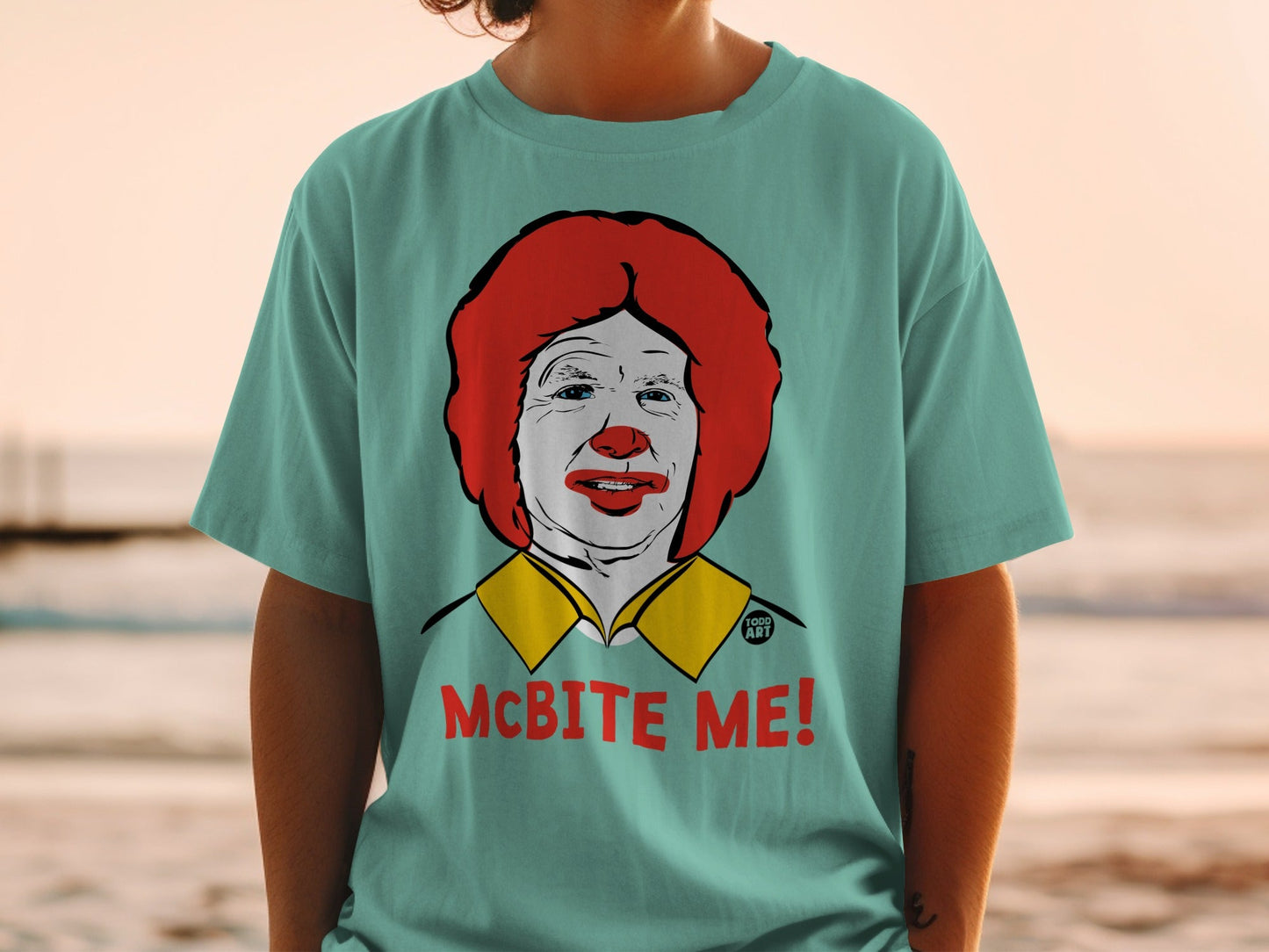Teal t-shirt with a cartoon portrait of Ronald McDonald and the text "MCBITE ME!".