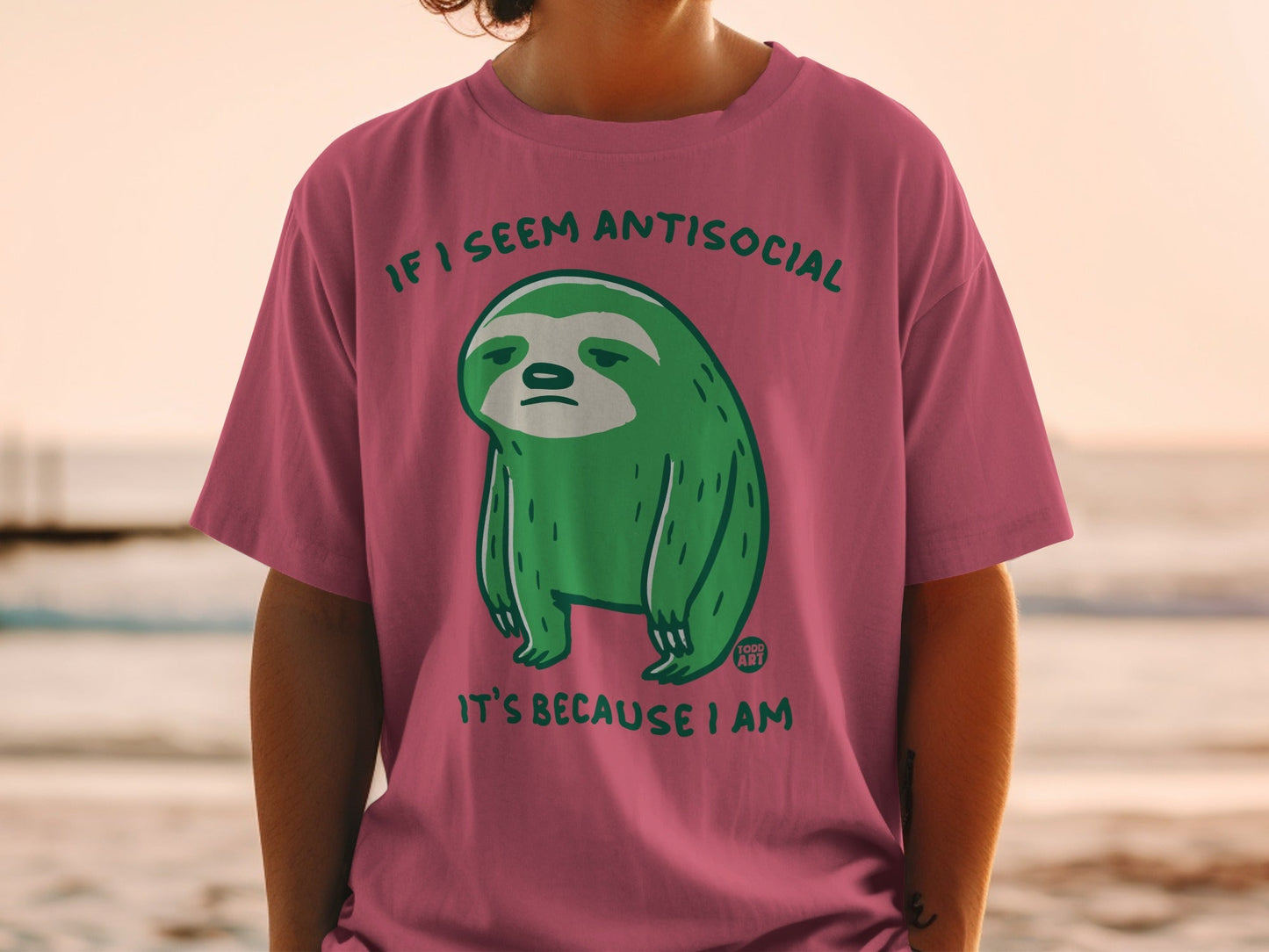 Green cartoon sloth on pink t-shirt reads "If I seem antisocial it's because I am."