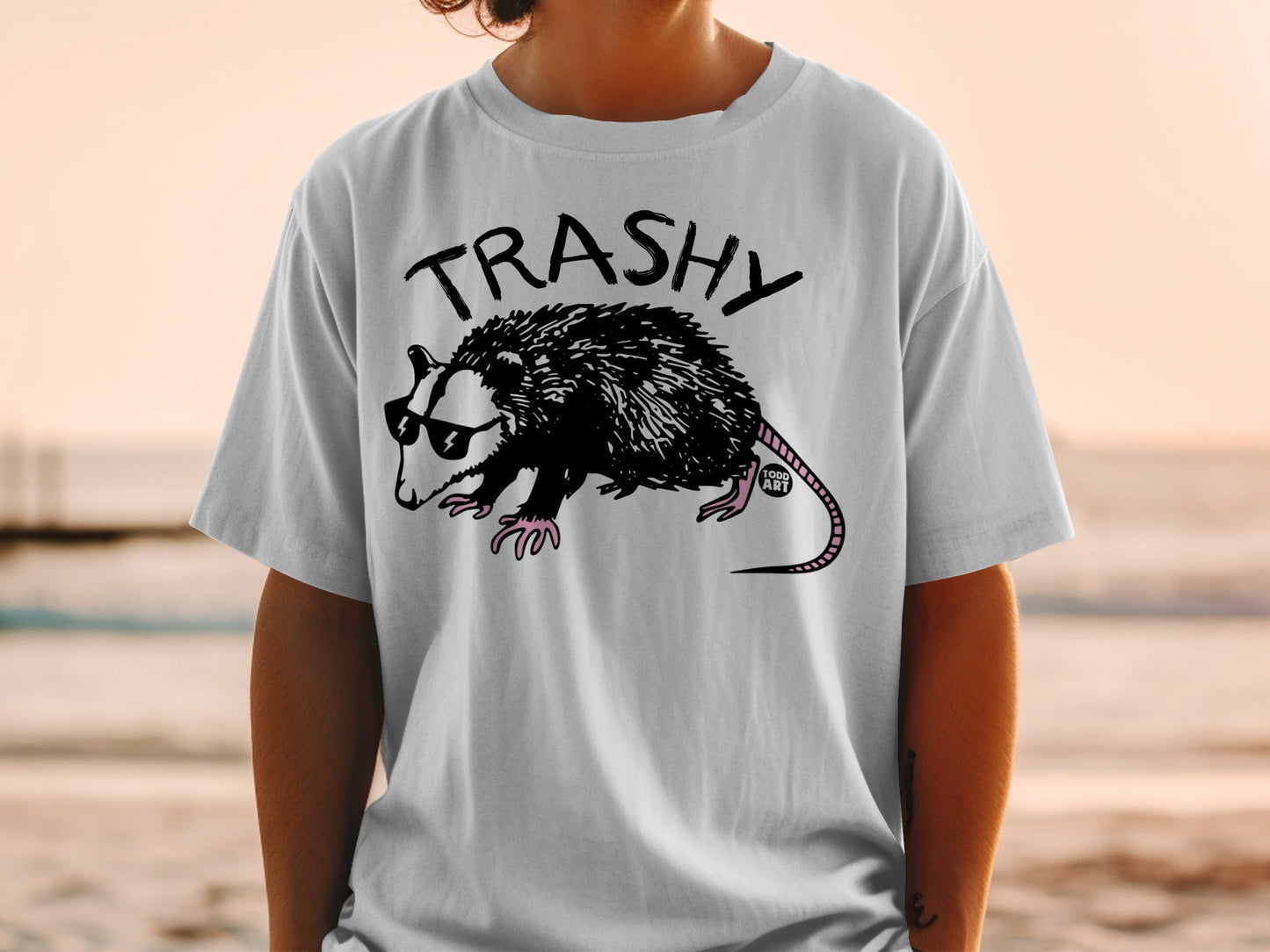 White t-shirt featuring a cartoon possum wearing sunglasses and the word "TRASHY".