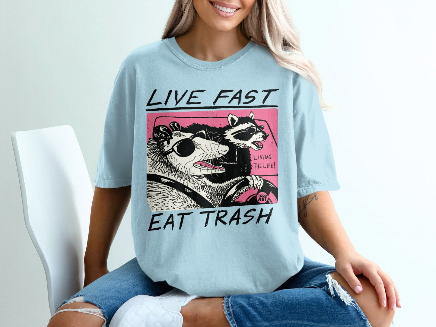 Light blue t-shirt with "LIVE FAST EAT TRASH" and possum/raccoon graphic.