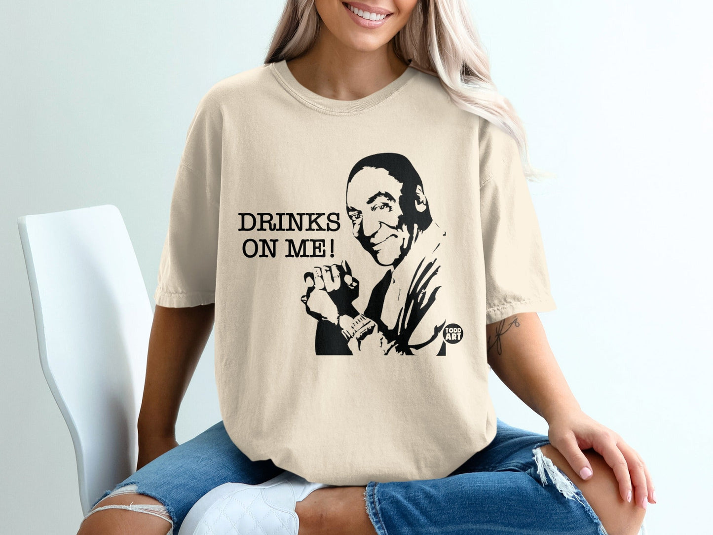 Cream t-shirt with black graphic of a smiling man and "DRINKS ON ME!" text.