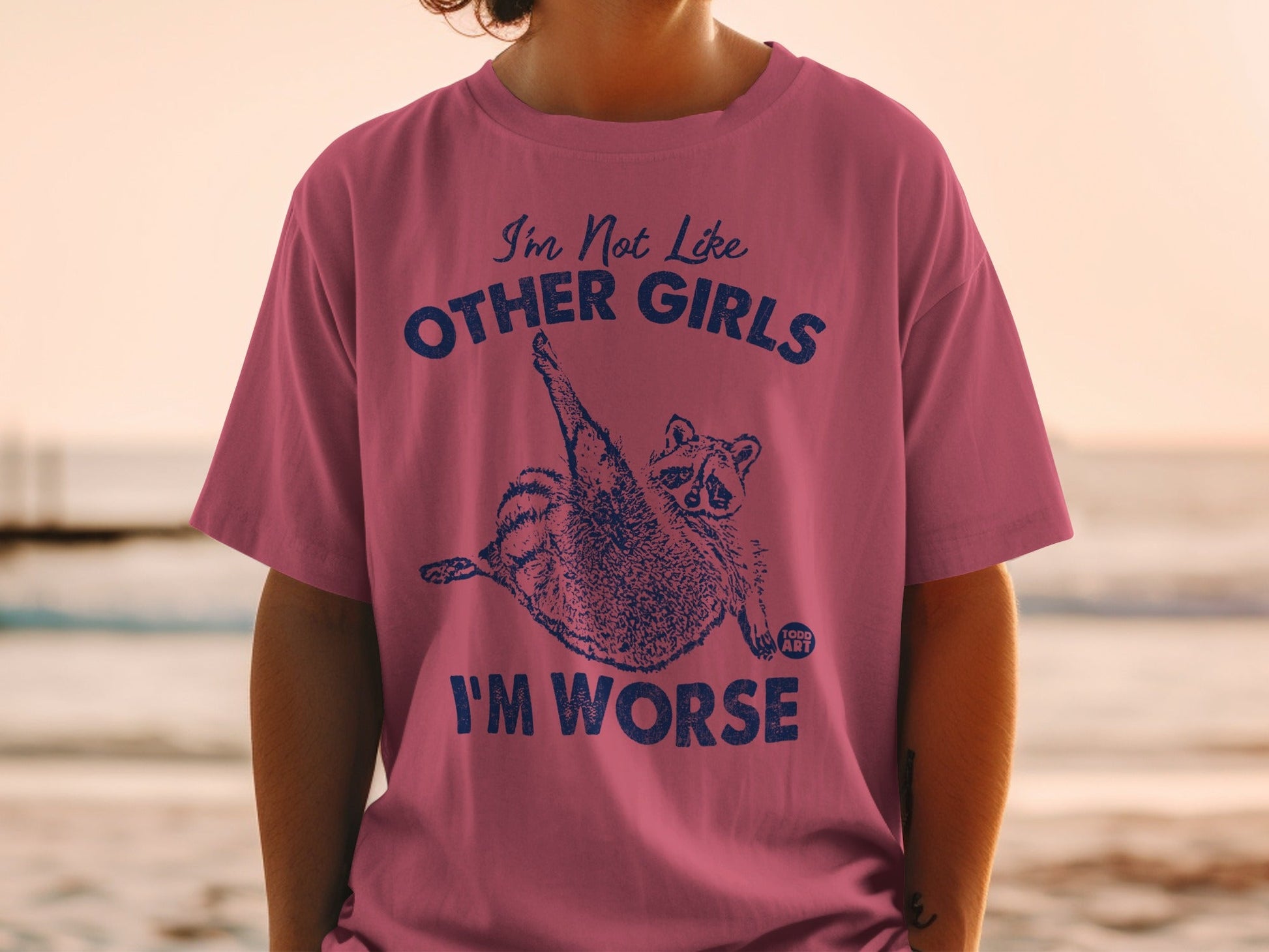 Pink t-shirt with raccoon graphic and "I'm Not Like Other Girls, I'm Worse" text.