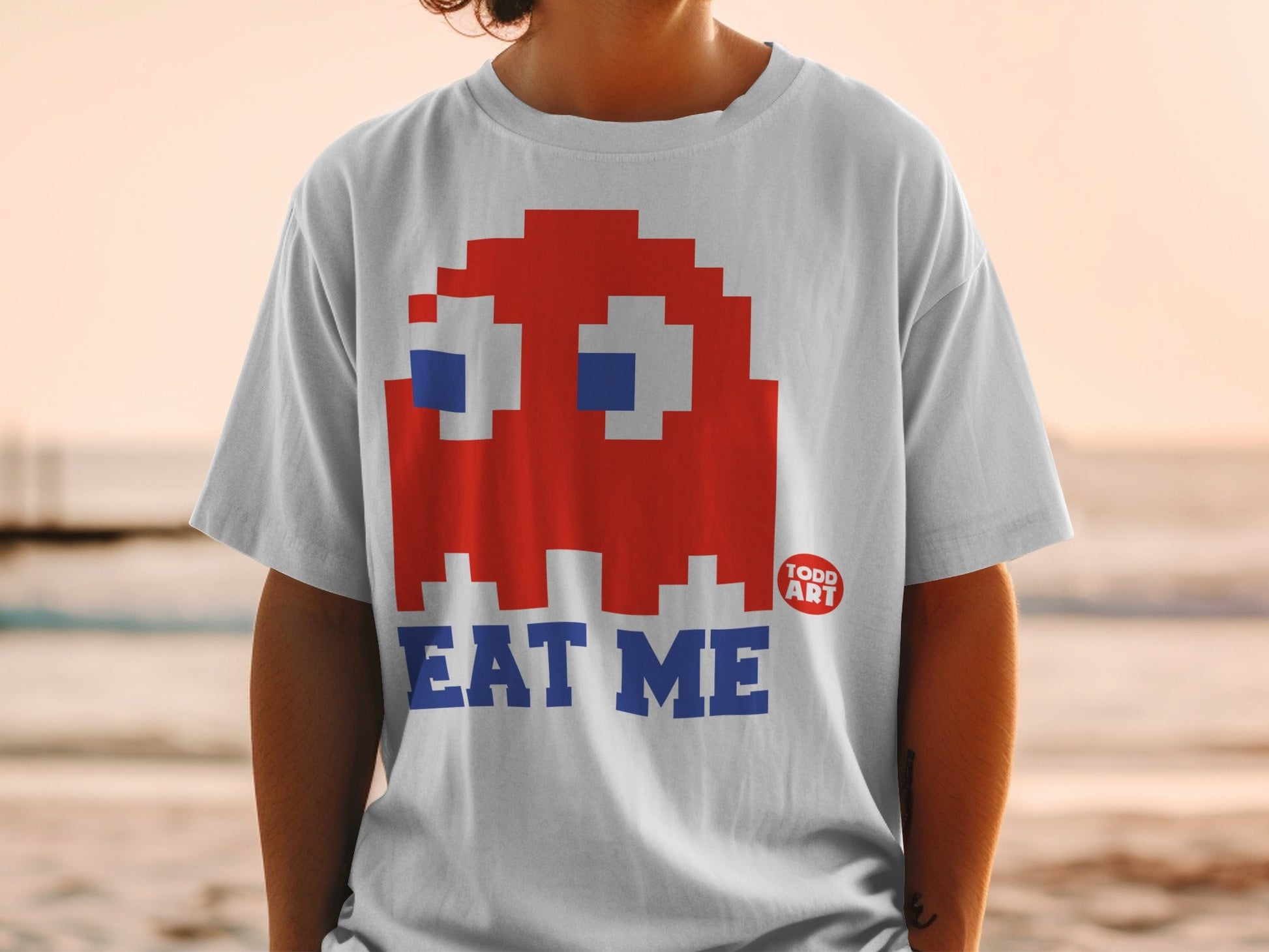 White t-shirt with red Pac-Man ghost and "EAT ME" text.