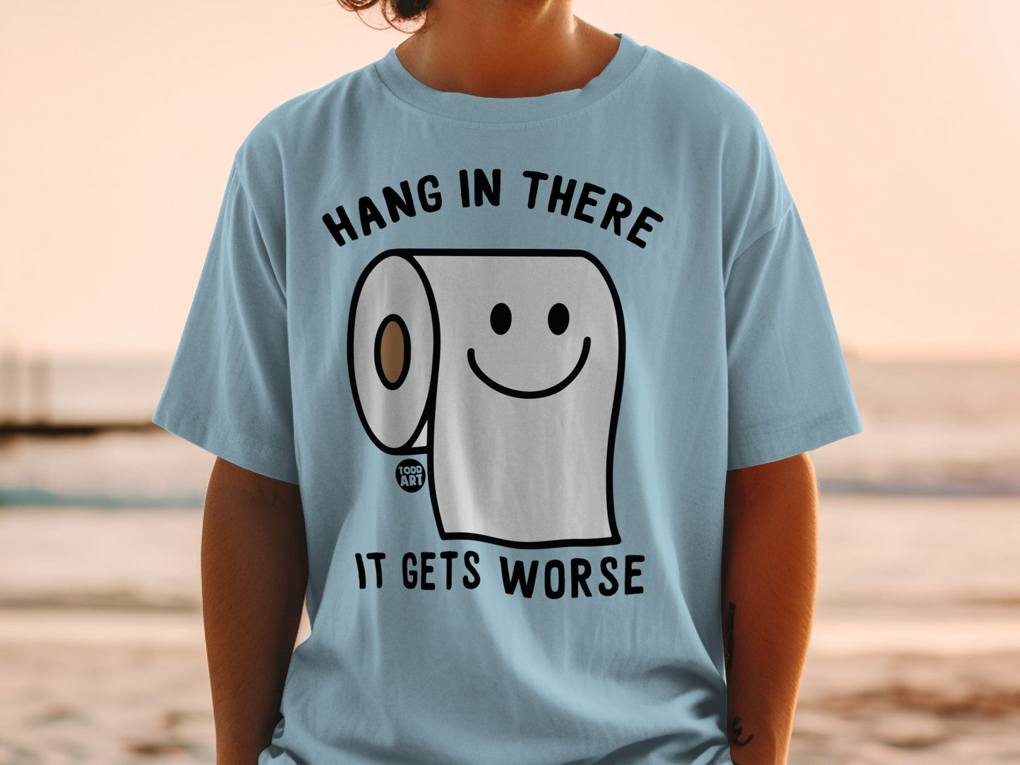 Light blue t-shirt with a smiling toilet paper roll and text "Hang in there, it gets worse".