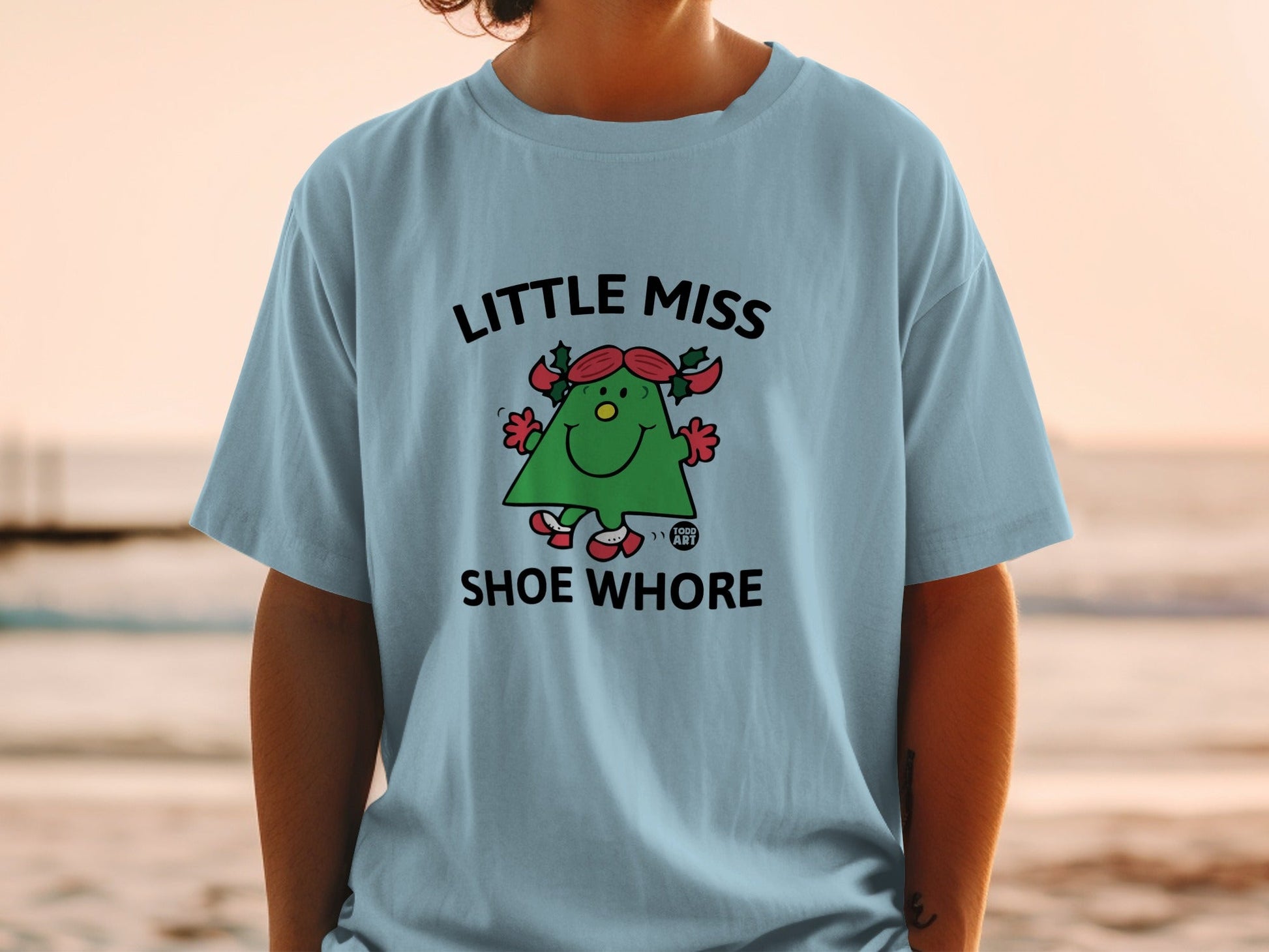 Light blue t-shirt with "Little Miss Shoe Whore" text and a cartoon character.
