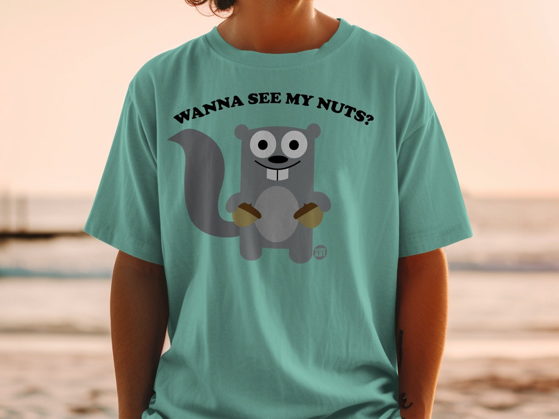 Teal t-shirt with a cartoon squirrel holding acorns and text "Wanna see my nuts?".