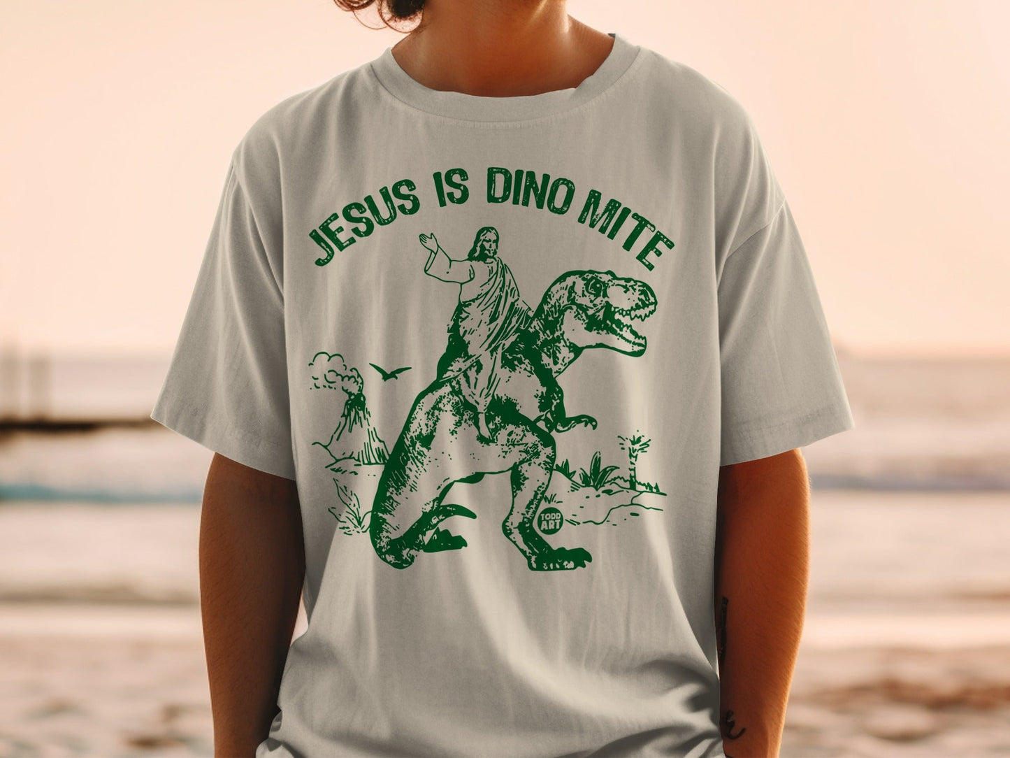 Jesus riding a T-Rex with "Jesus is Dino Mite" text and volcanoes.