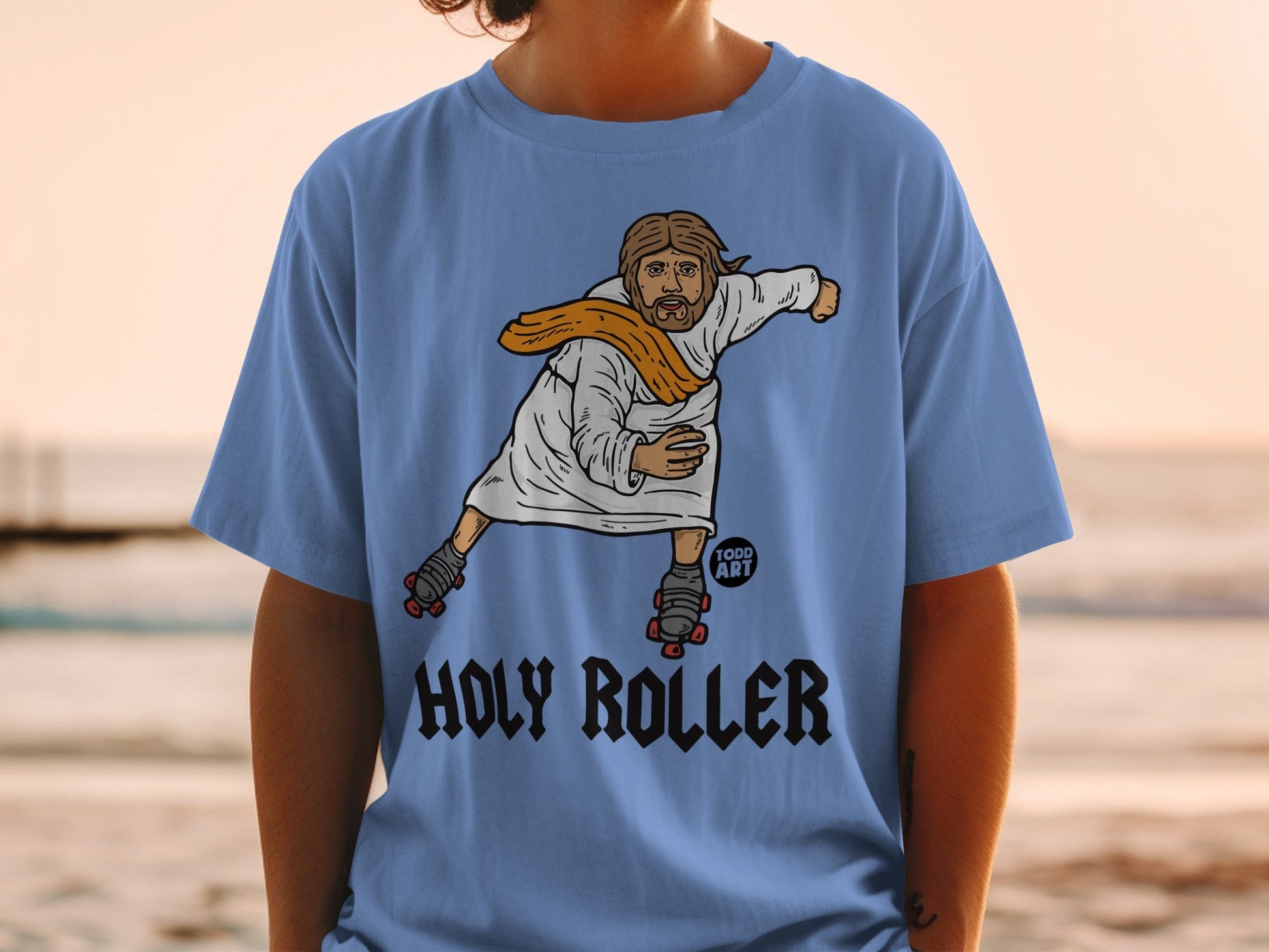 Light blue t-shirt featuring cartoon Jesus on roller skates with "HOLY ROLLER" text.