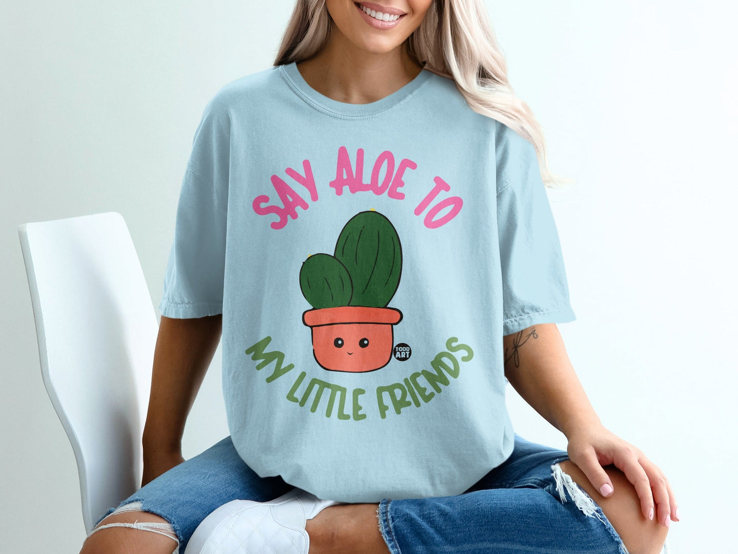 Light blue t-shirt with a cartoon cactus in a pot saying "Say aloe to my little friends".