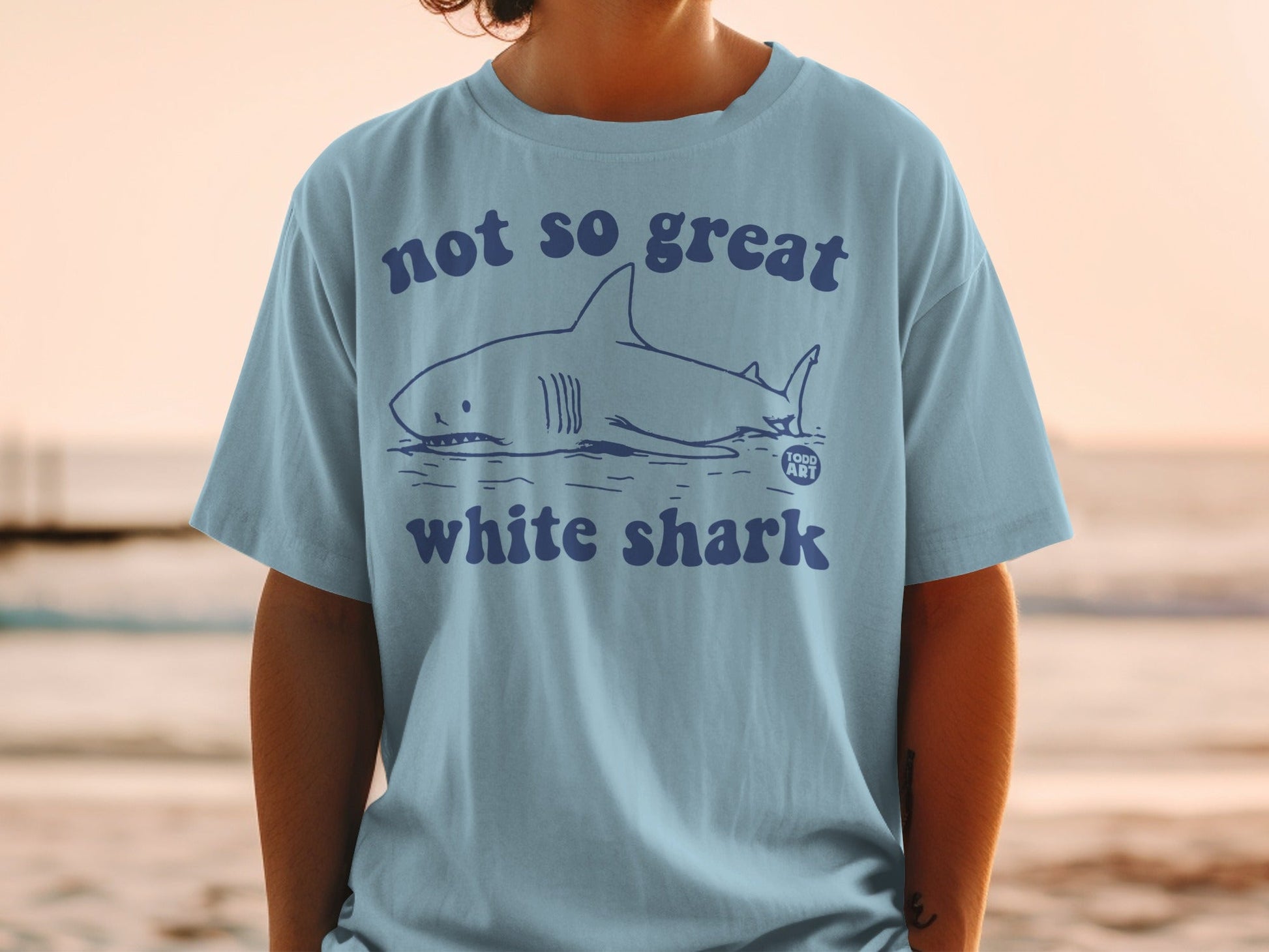 Light blue t-shirt with a graphic of a shark and "NOT SO GREAT white shark" text.
