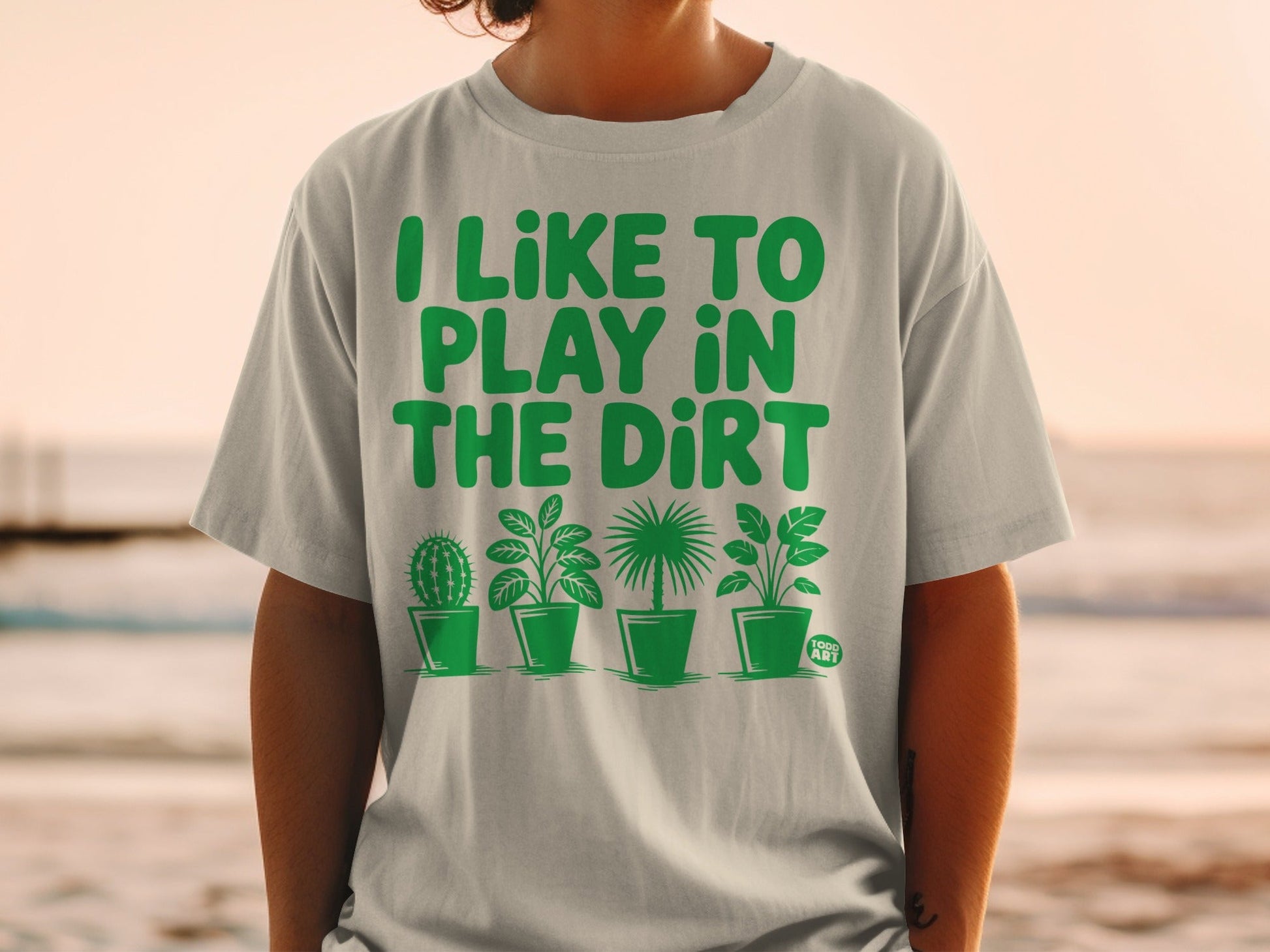 Gray t-shirt with green text "I LIKE TO PLAY IN THE DIRT" and potted plants.