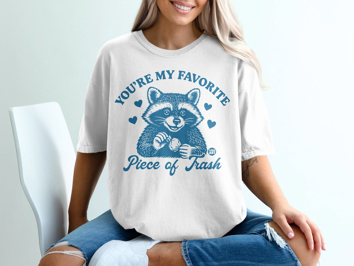 White t-shirt with raccoon illustration and "You're my favorite piece of trash" text.