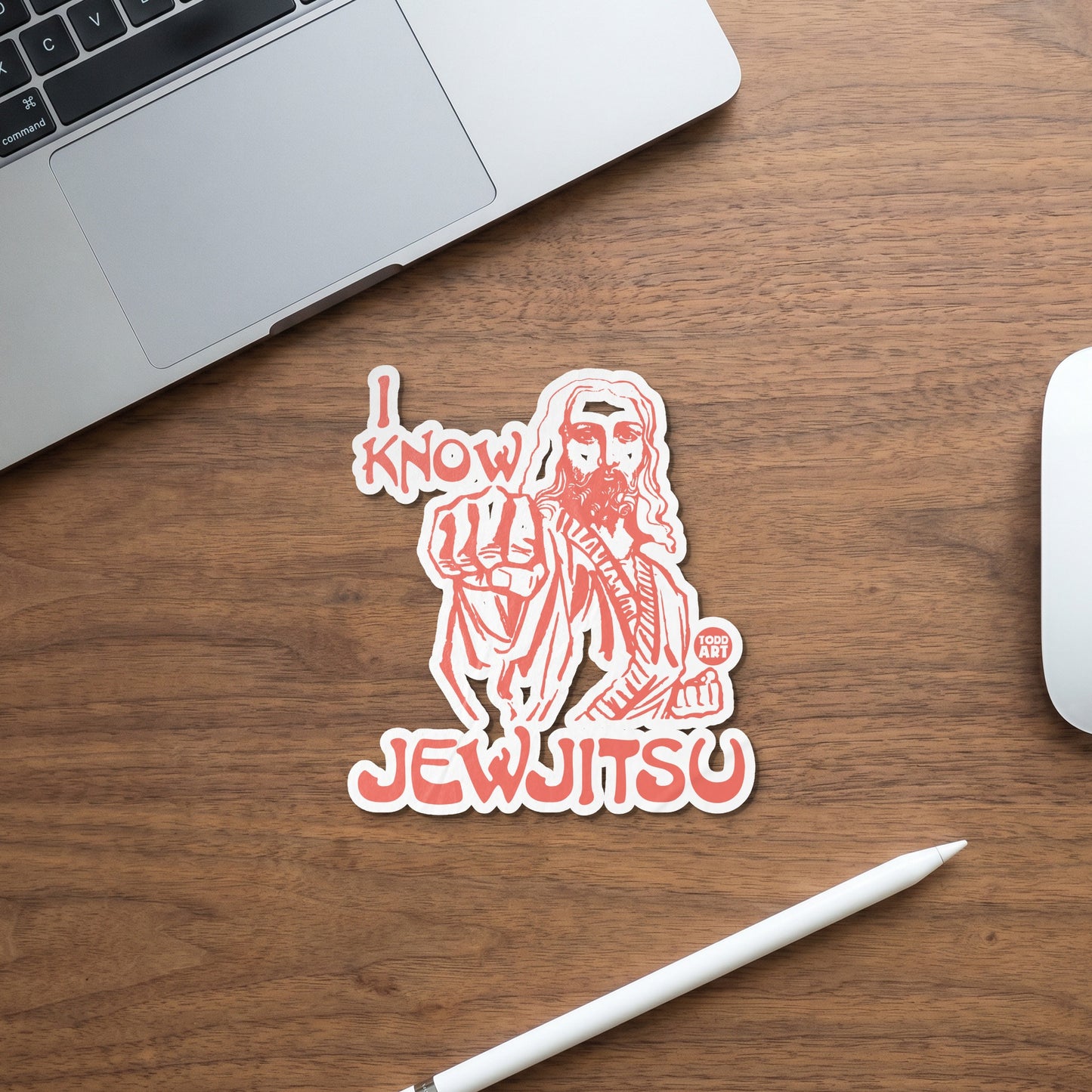 Jesus sticker with text "I Know JewJitsu" on wooden surface next to laptop.