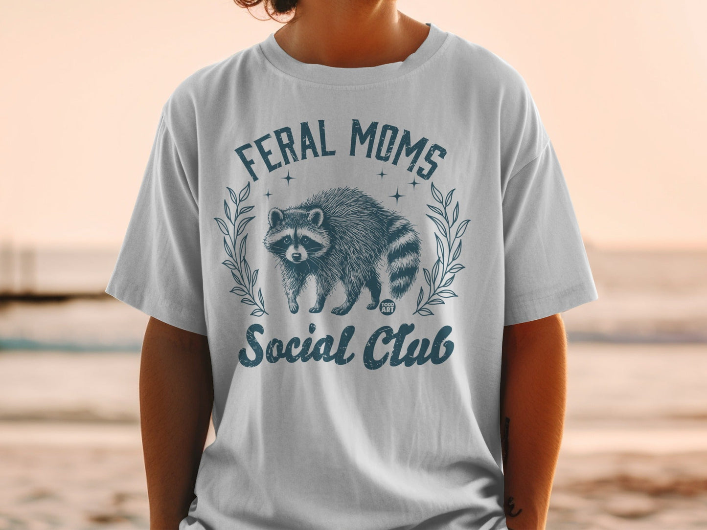 Feral Moms Social Club graphic with raccoon and laurel wreath on t-shirt.