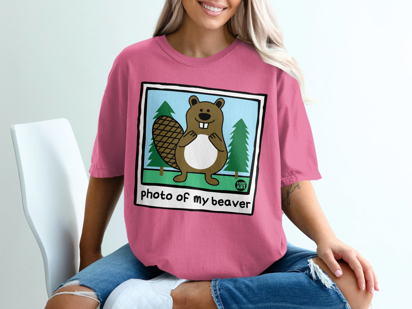 Pink t-shirt with a cartoon beaver and trees on a white background.