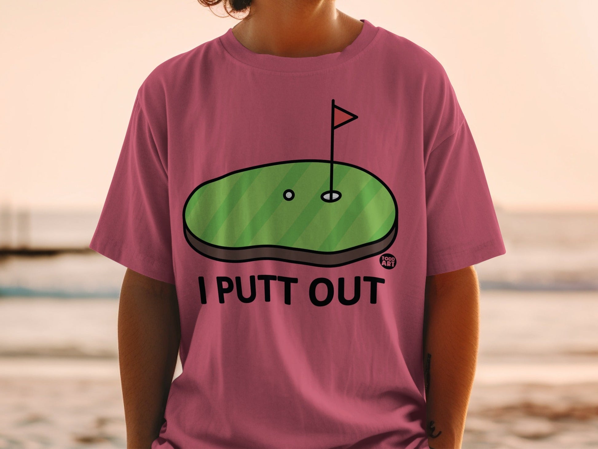 Pink t-shirt with "I PUTT OUT" and a golf putting green graphic.