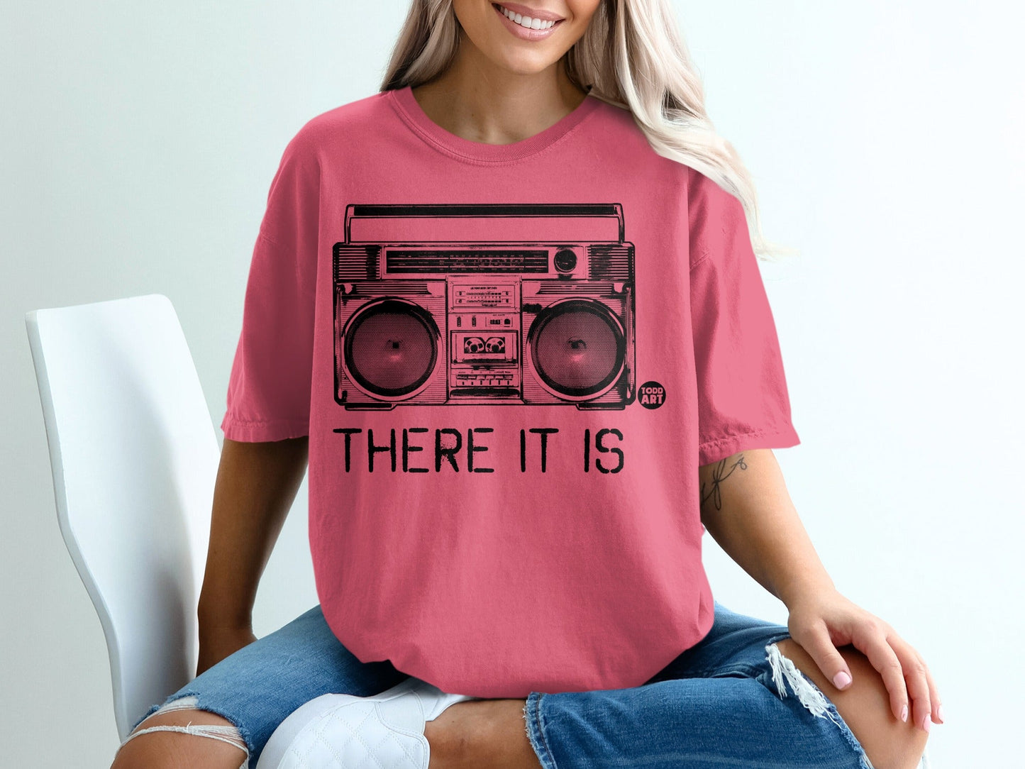 Pink t-shirt with a black graphic of a boombox and text "THERE IT IS".