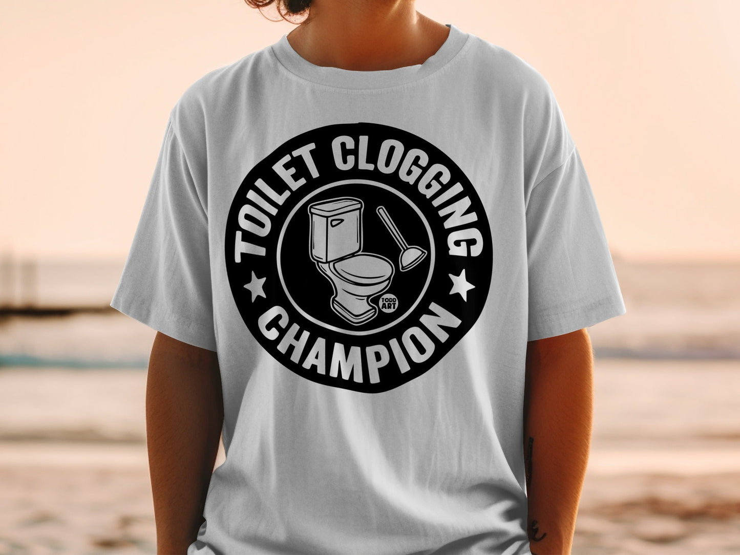 White t-shirt with black circular graphic of toilet and plunger, "Toilet Clogging Champion" text.