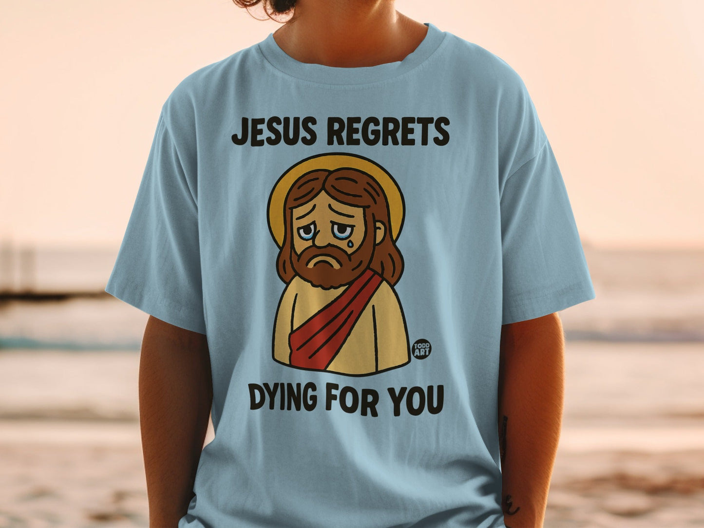 Light blue t-shirt with cartoon Jesus saying "Jesus regrets dying for you."