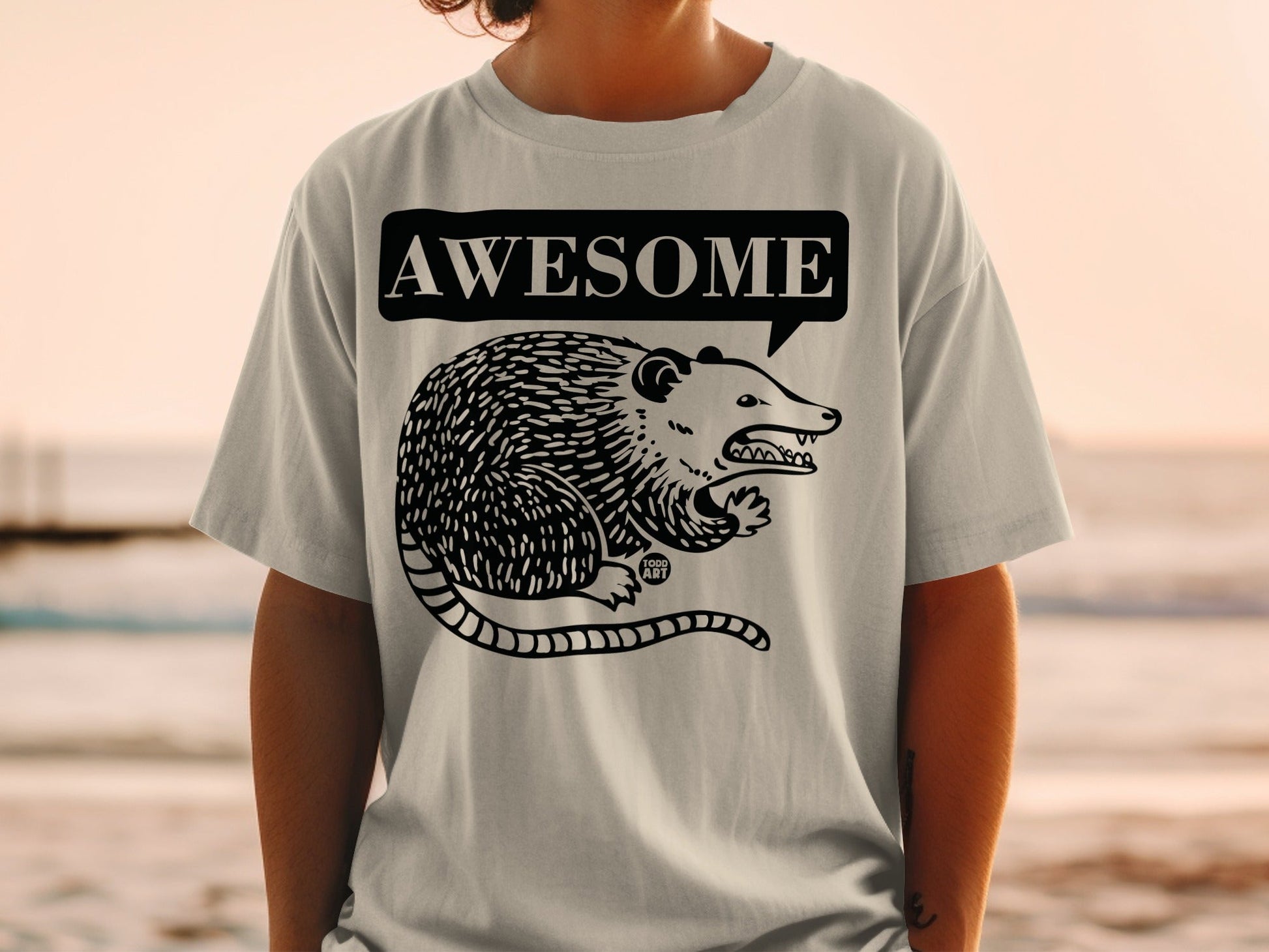 Gray t-shirt with black illustration of a possum in a speech bubble saying "AWESOME".