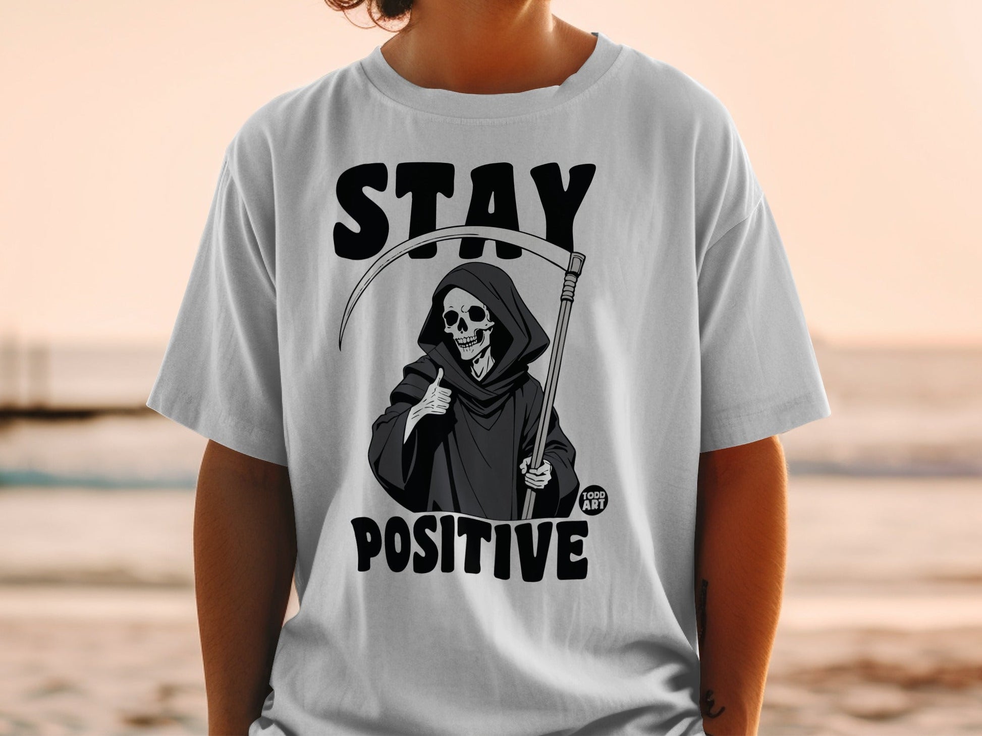 Grim Reaper graphic on t-shirt with "STAY POSITIVE" text.