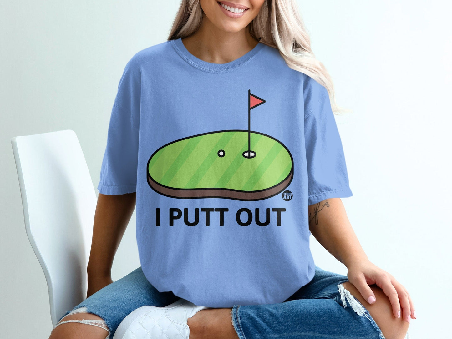 Light blue t-shirt with a golf green graphic and text "I PUTT OUT".