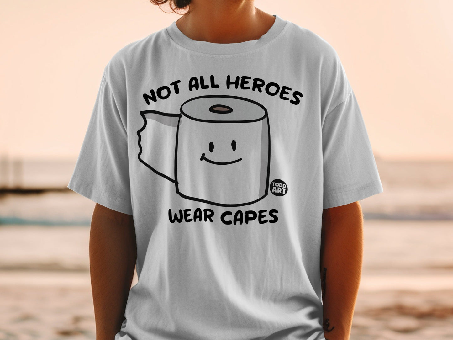 White t-shirt with toilet paper roll graphic and text "Not all heroes wear capes".